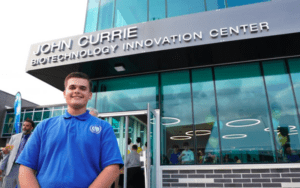 A PCTI student poses in front of the John Currie Biotechnology Innovation Center.