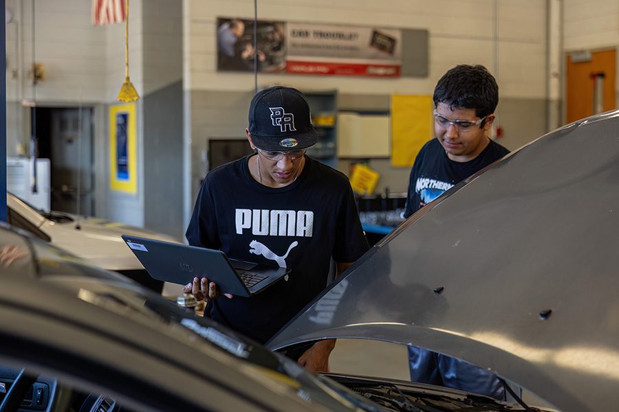 Two Passaic County students work under the hood of a car as part of their hands-on learning.