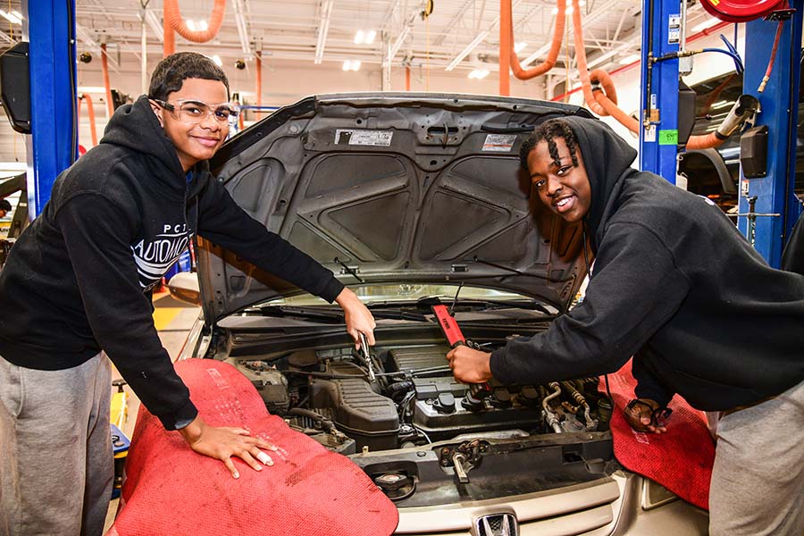 Two Passaic County students work under the hood of a car as part of their hands-on learning.