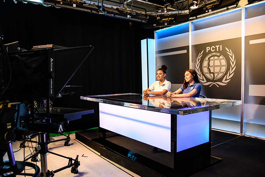 Passaic County students produce a TV broadcast behind an anchor desk in an on-campus studio.