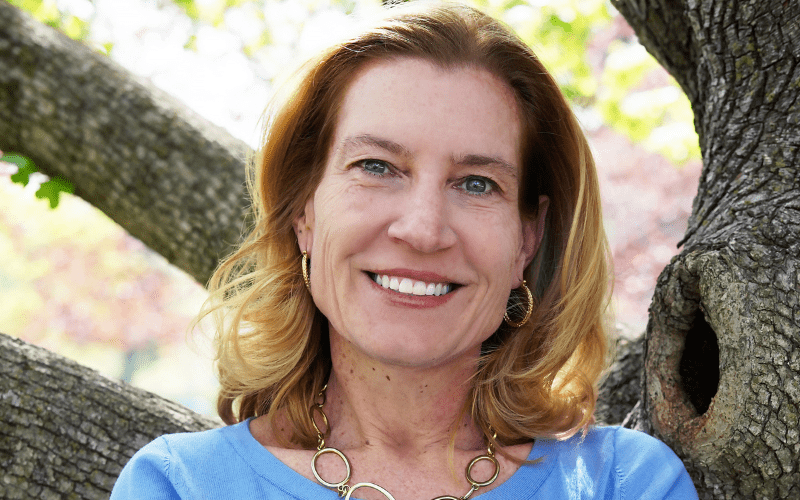 Jackie Burke smiling leaning on tree