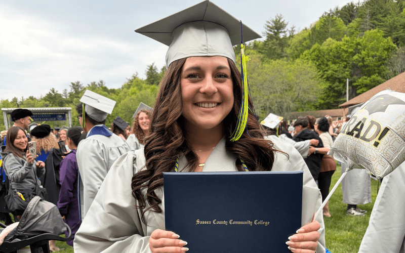 Student standing in with diploma in cap and gown